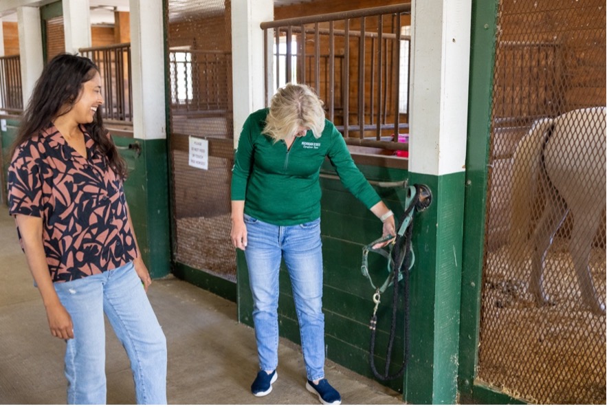 Lauren Enty and Karen Waite reading the words on a halter at MSU Horse Research & Training Center.